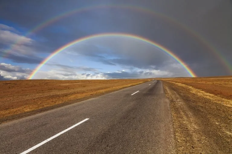 Lonely road in the desert under a rainbow