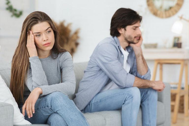 Upset young couple sitting on sofa at home, having conflict