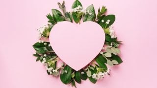 Tropical nature background with green leaves, white flowers and pink heart shaped paper for copy