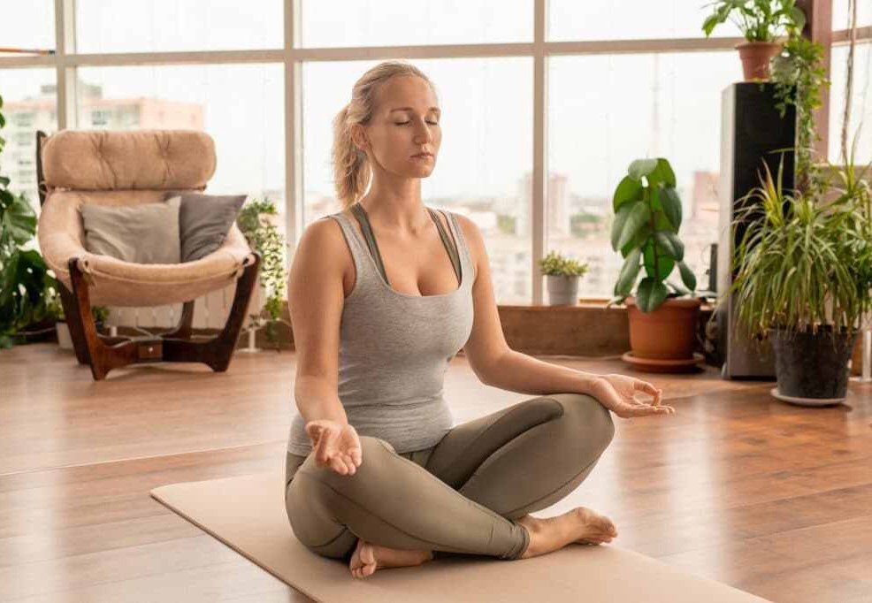 Young concentrated woman in sportswear crossing legs while sitting on mat