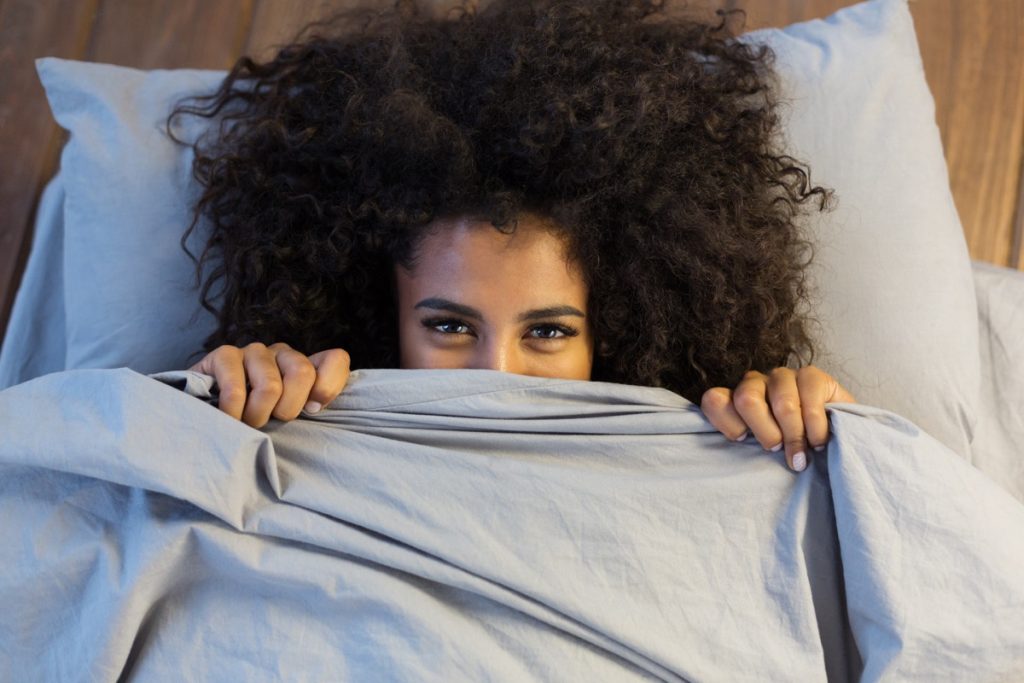 Beautiful african american woman smiling from behind her sheets and blankets